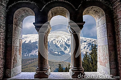 Beautiful gothic medieval arched stone window. Magnificent majestic view from the window. Winter mountains and a castle Stock Photo