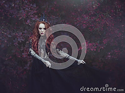 A beautiful gothic princess with pale skin and long red hair wearing a crown and a black dress against the backdrop of burgundy le Stock Photo