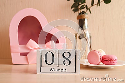 Beautiful greeting card for Women's Day. Wooden calendar 08 March, a glass of champagne, french macaroon pastry and a Stock Photo