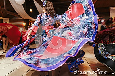 Beautiful gypsy girls dancing in traditional blue floral dress at wedding reception in restaurant. Woman performing romany dance Editorial Stock Photo