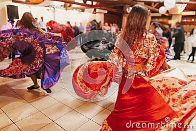 Beautiful gypsy girls dancing in traditional red floral dress at wedding reception in restaurant. Woman performing romany dance Editorial Stock Photo