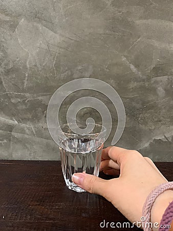 Beautiful hand of woman holding healthy mineral water in a clear glass on wooden table with cement wall, classic and vintage old s Stock Photo