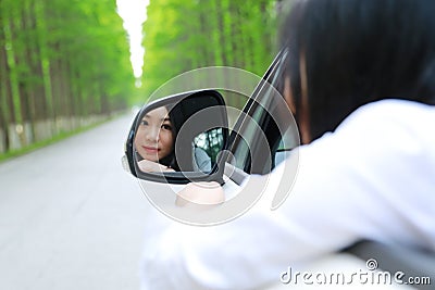 Beautiful happy Asian Chinese young woman sit on a white car look at herself from Automobile rearview mirror in summer safty drive Stock Photo