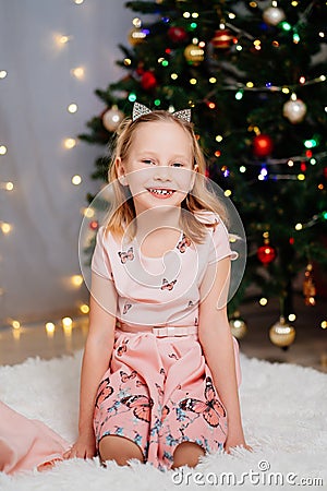 beautiful, happy blonde kid girl in pink dresses at the Christmas tree. Stock Photo