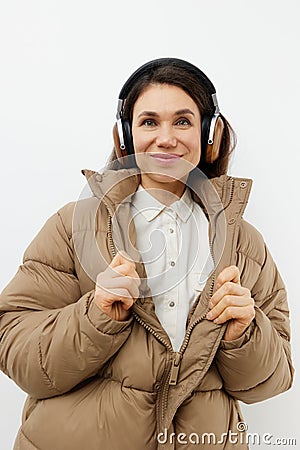 a beautiful happy brunette listens to music in brown headphones standing in a warm winter stylish jacket and smiles Stock Photo