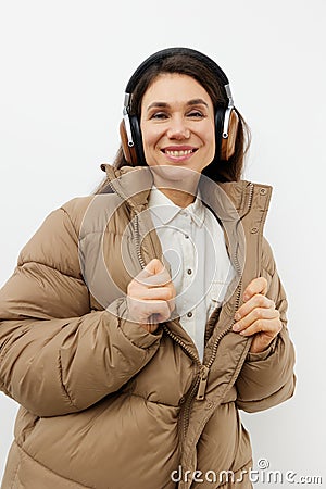 a beautiful happy brunette listens to music in brown headphones standing in a warm winter stylish jacket and smiles Stock Photo