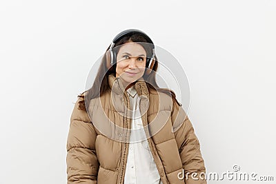 beautiful, happy, brunette listens to music in brown headphones, standing in a warm winter, stylish jacket and smiling Stock Photo