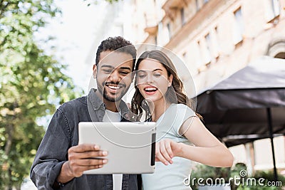 Beautiful happy couple using digital tablet. Joyful smiling woman and man looking at gadget in city street in summer Stock Photo