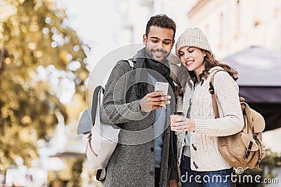 Beautiful happy couple using smartphone. Young joyful smiling woman and man looking at mobile phone in a city in autumn. Technolo Stock Photo