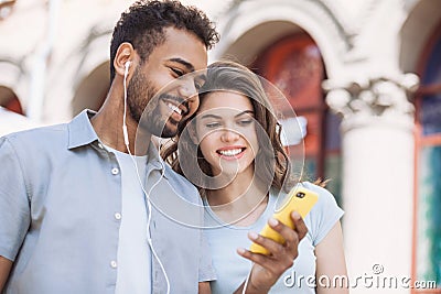 Beautiful happy couple using smartphone. Young joyful smiling woman and man looking at mobile phone in a city. Technology, travel Stock Photo