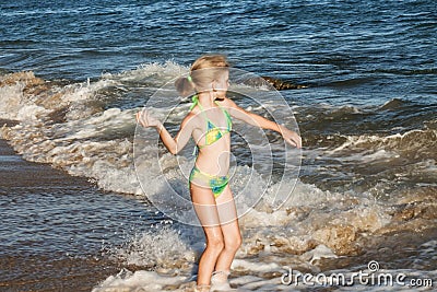 Beautiful and happy girl in a green swimsuit throws a pebble in the sea, beach concept Stock Photo