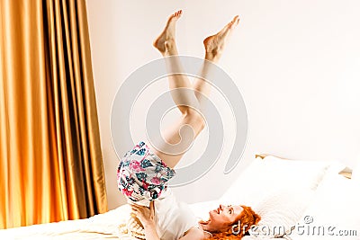 Beautiful happy girl lying on bed in light bedroom in the morning, make some exercice. Stock Photo
