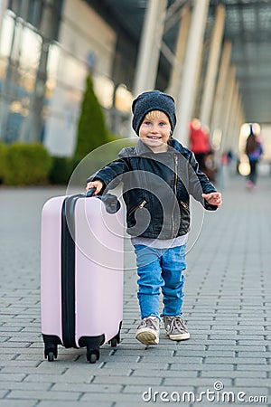 Beautiful happy girl travels with stylish suitcase. Little child traveler goes to the trip from airport. Stock Photo