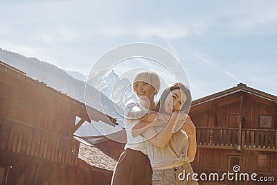 beautiful happy girls hugging while standing between wooden houses in mountain village mont Stock Photo