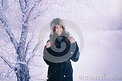 Beautiful happy laughing young woman wearing winter hat gloves covered with snow flakes. Stock Photo