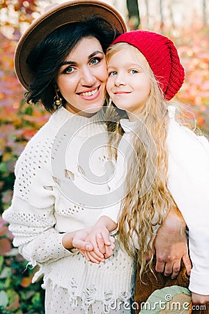 Beautiful and happy mother and daughter in the autumn forest, mother hugs and kisses the girl, colorful leaves on the trees Stock Photo
