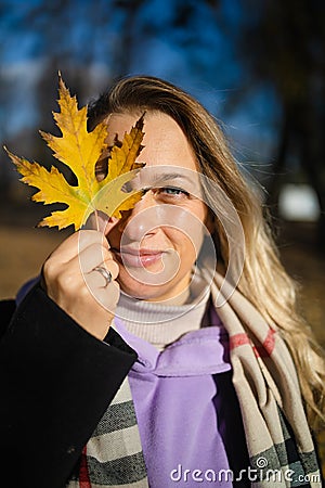 Middle aged woman with a smile holds an autumn yellow leaf near the face Stock Photo