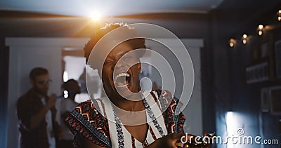 Beautiful happy young African woman laughing, blowing on confetti at fun atmospheric celebration party slow motion. Stock Photo