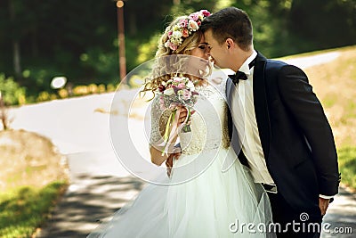 Beautiful happy young bride kissing handsome groom in sunlit par Stock Photo