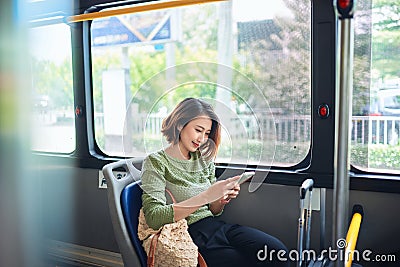 Beautiful happy young woman sitting in city bus, looking at mobile phone Stock Photo