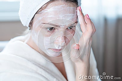 Happy woman applying cream on face moisturizing the skin. Concept of hygiene and care for the skin at home Stock Photo