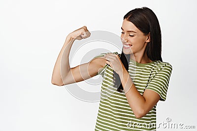 Beautiful and healthy athletic woman, showing muscles, flexing bicep and smiling, looking at her strong arm, standing Stock Photo