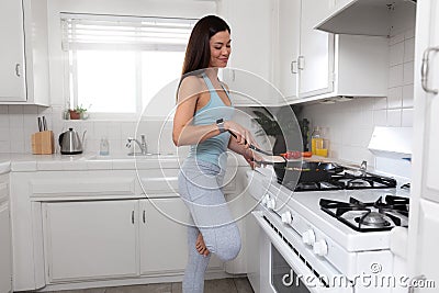 Beautiful healthy fit and toned woman cooking a plant based diet meal in a bright kitchen, after a exercise workout, nutrition and Stock Photo