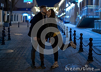 Beautiful heterosexual couple is on the path of cobblestones and kiss. On the background of a city street Stock Photo