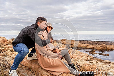 Beautiful heterosexual mixed race couple outdoor live a tenderness moment sitting on sea resort rocks - Caucasian handsome guy Stock Photo