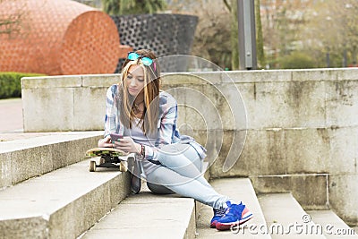 Beautiful hipster urban girl with skateboard and cellphone. Stock Photo