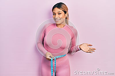 Beautiful hispanic woman using tape measure measuring waist celebrating achievement with happy smile and winner expression with Stock Photo