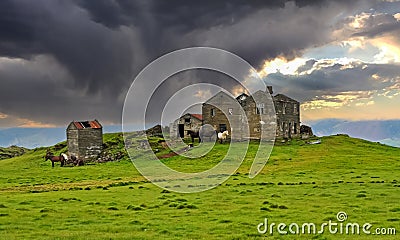 Beautiful icelandic lonely quiet rural landscape, abandoned old idyllic farm house ruin on green hill with herd horses, dark storm Stock Photo