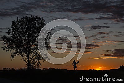 Beautiful image of a silhouette of lady standing close to a tree and reading a book Stock Photo