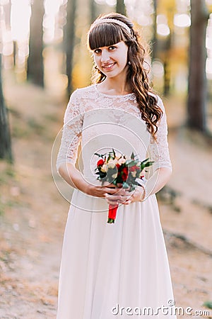 Beautiful innocent young brunette bride in gorgeous white dress with bouquet of flowers at forest Stock Photo