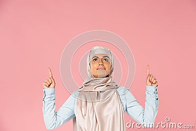 Islamic woman in hijab pointing up, isolated on pink Stock Photo