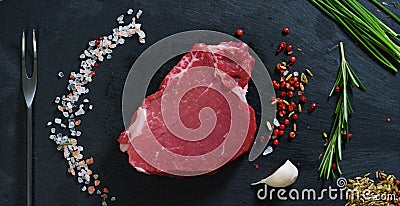 Beautiful juicy fresh meat steak on a table with salt, rosemary, garlic, and tomato on a black background, top view. Concept: fres Stock Photo