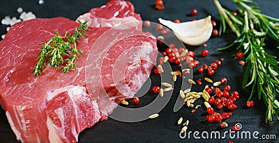 Beautiful juicy fresh meat steak on a table with salt, rosemary, garlic, and tomato on a black background, top view. Concept: fres Stock Photo