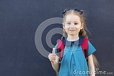 Kid back to school. Happy pupil girl standing at blackboard with chalk in hand. cute confident schoolgirl with backpack i Stock Photo