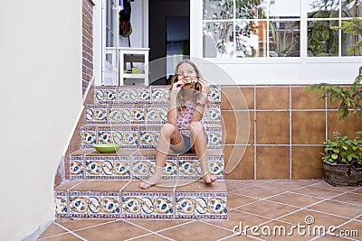 Beautiful kid girl eating watermelon on stairs at home. Family love and lifestyle outdoors Stock Photo