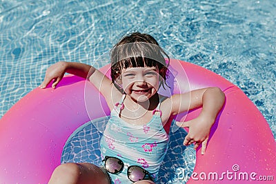 beautiful kid girl floating on pink donuts in a pool. Wearing sunglasses and smiling. Fun and summer lifestyle Stock Photo