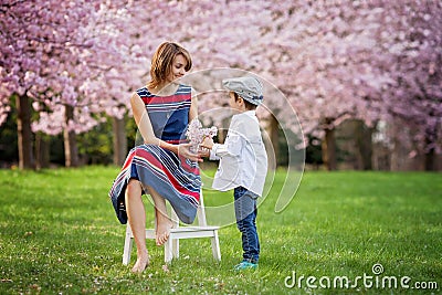 Beautiful kid and mom in spring park, flower and present. Mother Stock Photo