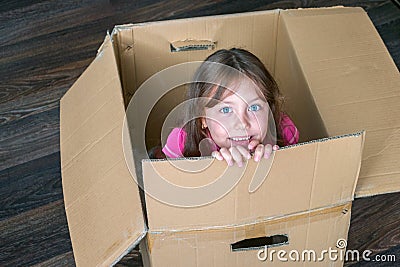 Beautiful kid sits in a mail box. A little girl is in a cardboard box. Baby moves to a new apartment. The child plays funny. Stock Photo