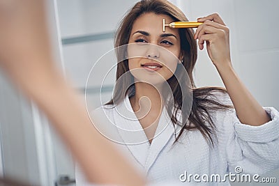Charming young woman using golden facial massager Stock Photo