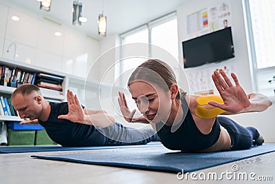 Beautiful lady in sportswear with yellow tape on shoulder practicing locust yoga pose Stock Photo