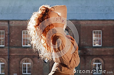 Beautiful lady with sunlight highlighting cascading long wavy red hair, hand holding hair on top of her head Stock Photo