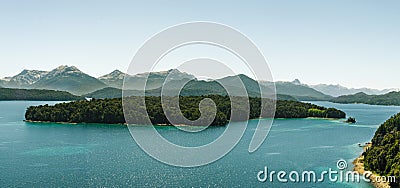 Beautiful lake with intense turquoise shores, a wooded island in the middle and snowy mountain ranges in the background Stock Photo