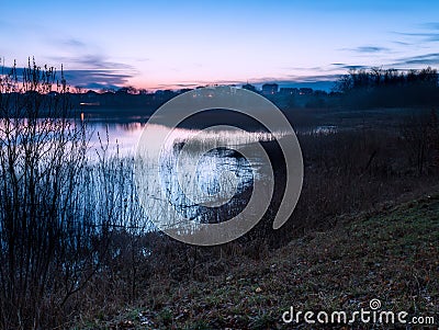 Beautiful lake near city with colorful sunset sky. Tranquil vibrant landscape Stock Photo