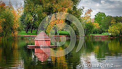 Beautiful lake with small wooden houses for ducks and autumn willow trees with green, yellow leaves in city park. Moscow Stock Photo