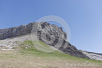 Beautiful landscape, green meadow leading up to mountain cliff. Stock Photo