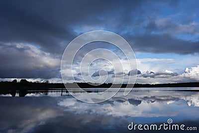 Beautiful landscape with high mountains with illuminated peaks, stones in mountain lake, reflection, blue sky and yellow sunlight Stock Photo